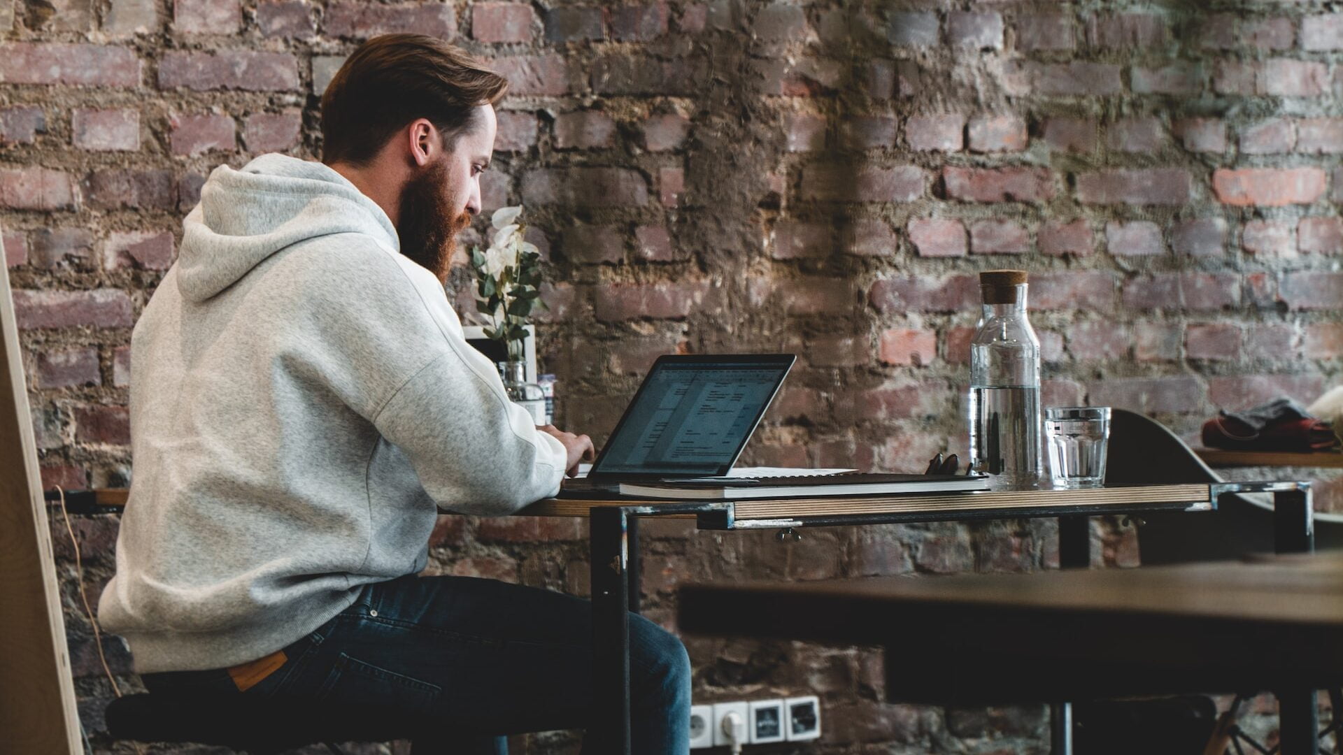 man in beige hoodie sitting on chair using laptop computer being nomad